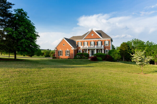 Front of home and garage of large single family modern US house with landscaped gardens and lawn on a warm sunny summers day
